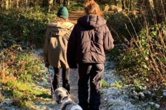 two young girls out walking a dog in the woods in winter