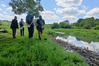 A group of volunteers standing on a riverbanks looking at a river on a sunny day