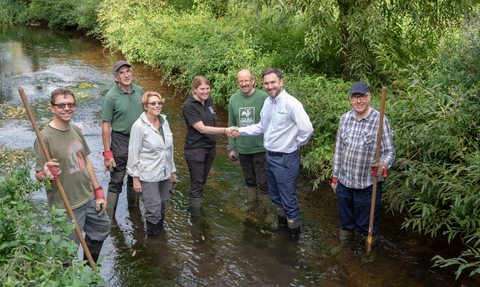 A group of people wearing wellies standing in a river holding rakes and smiling