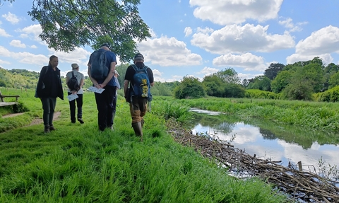 A group of volunteers standing on a riverbanks looking at a river on a sunny day