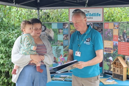 Man in blue top talking with woman holding her young child