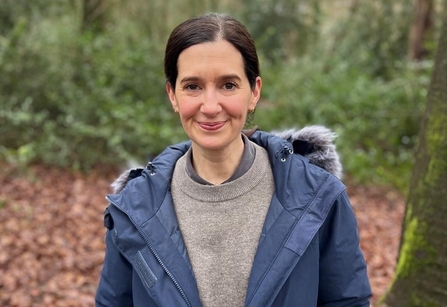 Woman in blue coat and grey jumper standing in woodland in winter