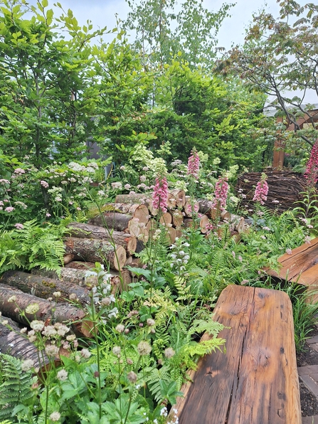 A pile of neatly stacked logs amongst lush greenery and wildlflowers in a garden 